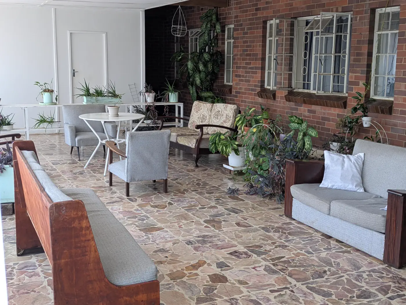 The veranda at Fenella Redrup: sofas, armchairs and pot plants along a red-brick wall