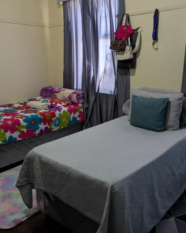 A shared room with two single beds, grey curtains and a soft rug